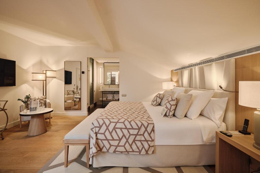 Luxurious hotel room with a large king bed, geometric throw, and matching pillows facing a wooden headboard and bedside lamps.
