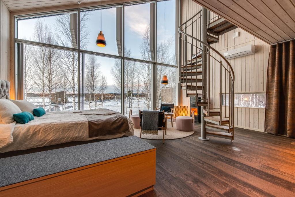 Spacious hotel suite with a large bed, teal pillows, and floor-to-ceiling windows overlooking a snowy landscape.