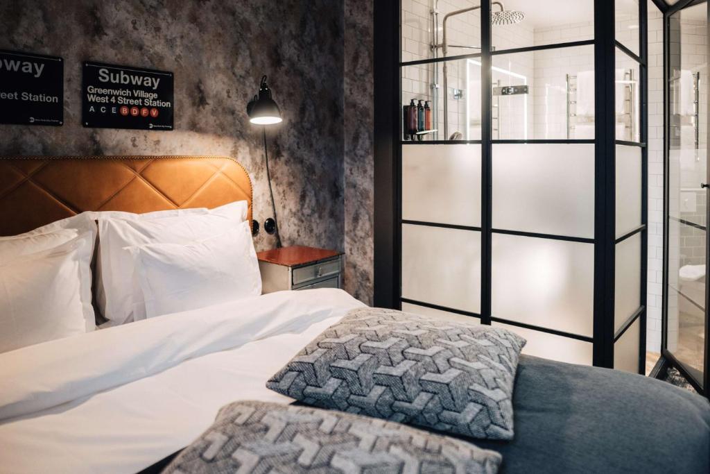 Hotel bedroom with a large bed, white linens, and patterned throw pillows beside a glass-walled bathroom.