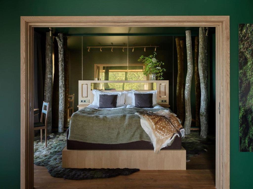 Bedroom framed by a wooden doorway, featuring a large bed with gray bedding and a deer-pattern throw, green walls, and log-like pillars surrounding the bed