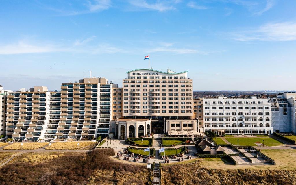 A large seaside hotel complex with a central white building labeled Huis ter Duin, facing a sandy promenade.