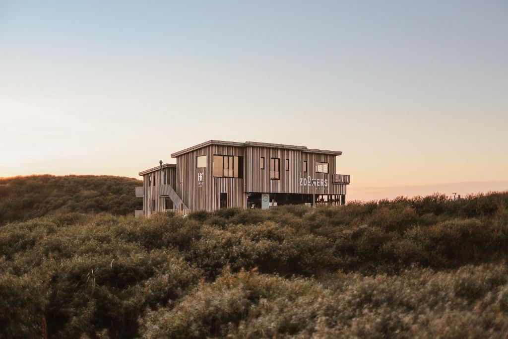 Wooden coastal house on stilts in a shrub-covered dune at sunset.