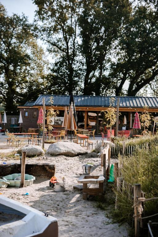 Outdoor cafe with wooden tables under umbrellas, sandy yard in front and trees behind behind.