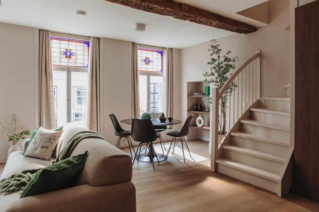 Bright open living and dining area with a beige sofa, round glass table, black chairs, and tall windows with stained glass accents near a curved white staircase.