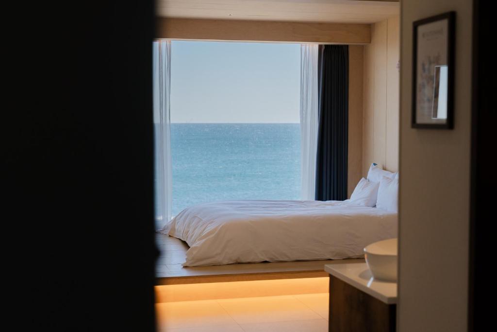 Bed with white bedding facing a large window showing a blue sea outside