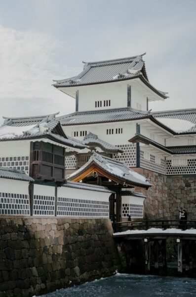 White Japanese castle with snow-covered tiled roofs beside a stone wall and moat