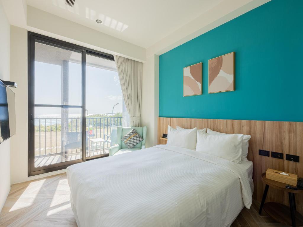Hotel room with a white bed, teal accent wall, and sliding glass doors to a balcony