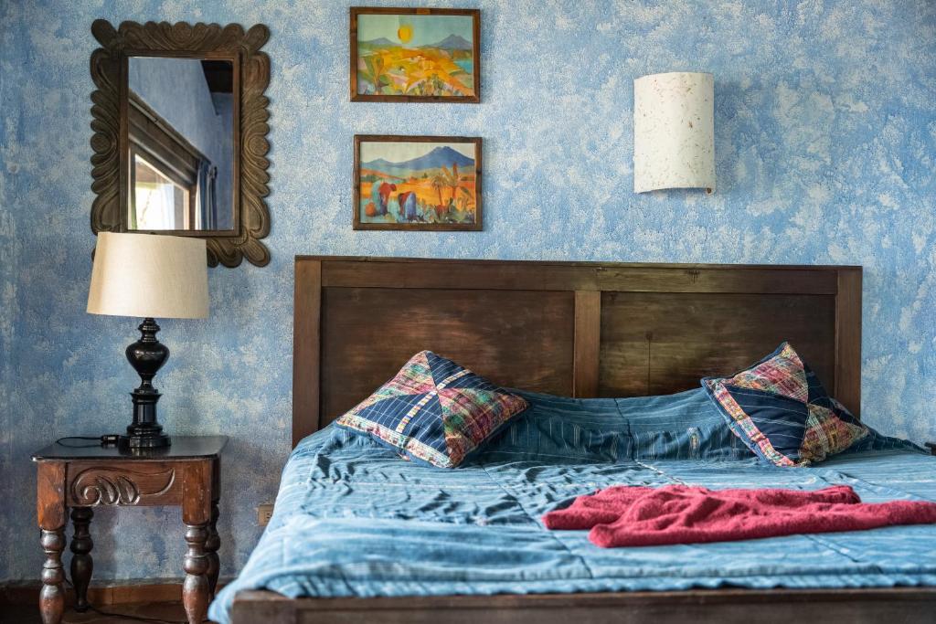 Rustic bedroom with a dark wood bed, blue bedding, and two plaid pillows against a blue textured wall, with a red throw on the bed.