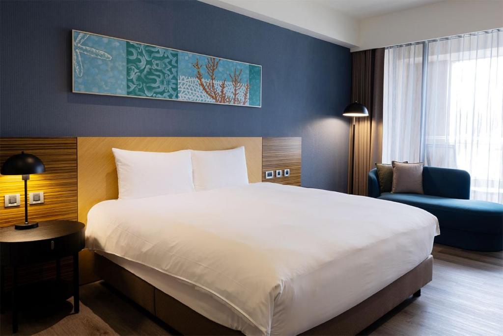 King-size bed with white linens and two pillows against a wooden headboard on a navy accent wall, with bedside lamp and round table.