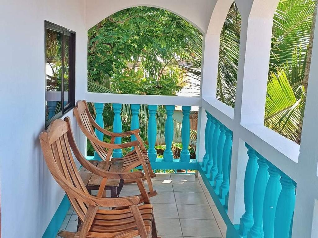 Sunlit balcony with turquoise blue railing and wooden rocking chairs, overlooking lush tropical plants.