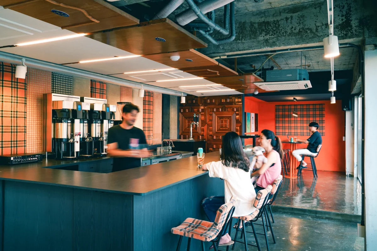 Café interior with a long dark counter, plaid bar stools, and people sitting and chatting at the bar.