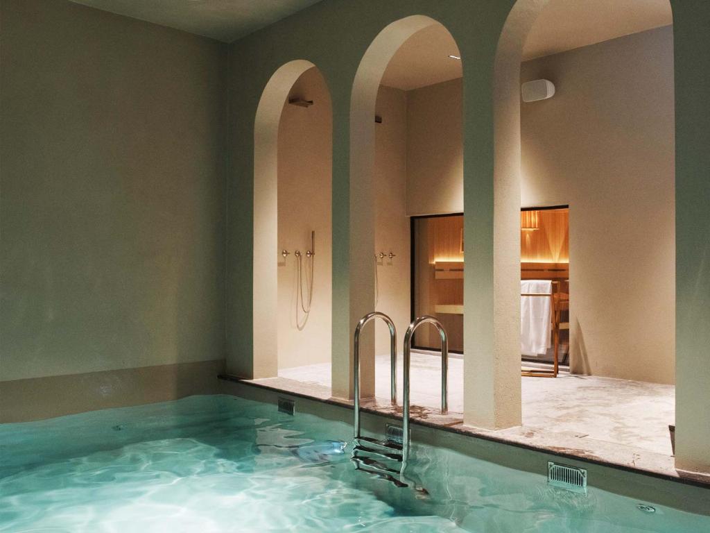 Indoor pool with turquoise water, a metal ladder, and three beige arched alcoves leading to a shower/locker area.