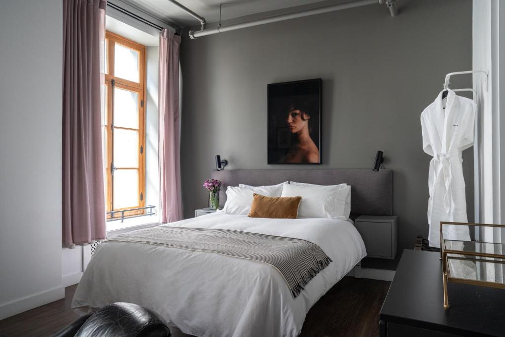 Bright hotel-style bedroom with white bedding, gray headboard, mustard throw pillow, and a portrait on a gray wall.