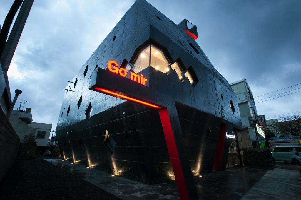 Angular black building at dusk with red neon sign 'Go mir' and diamond-shaped windows on a corner.