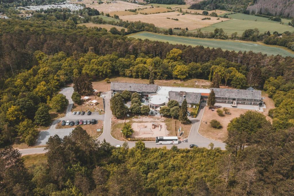 Aerial view of a wooded campus with two long buildings, a central circular area, a playground, and a parking lot with cars nearby.