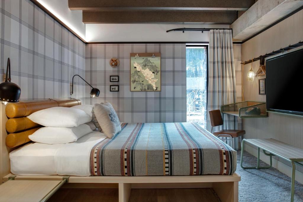 Bedroom with a large bed and striped blanket, plaid walls, and wall-mounted lamps; a work desk and chair sit by a window in the corner.
