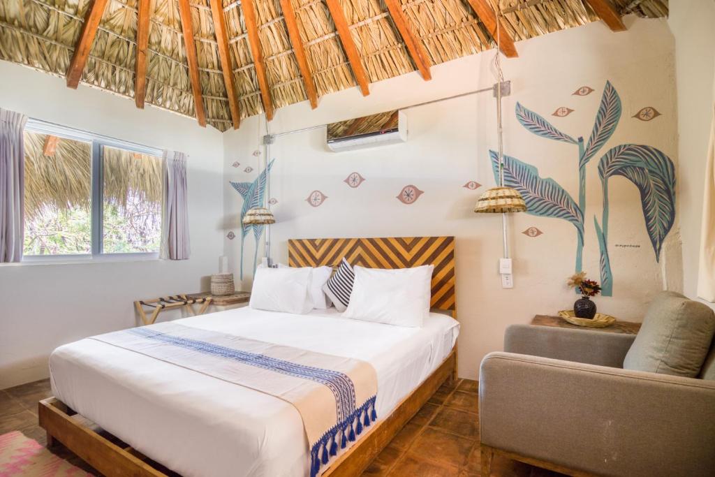 Hotel room with a thatched ceiling, king bed, and blue leaf mural on the wall behind the bed