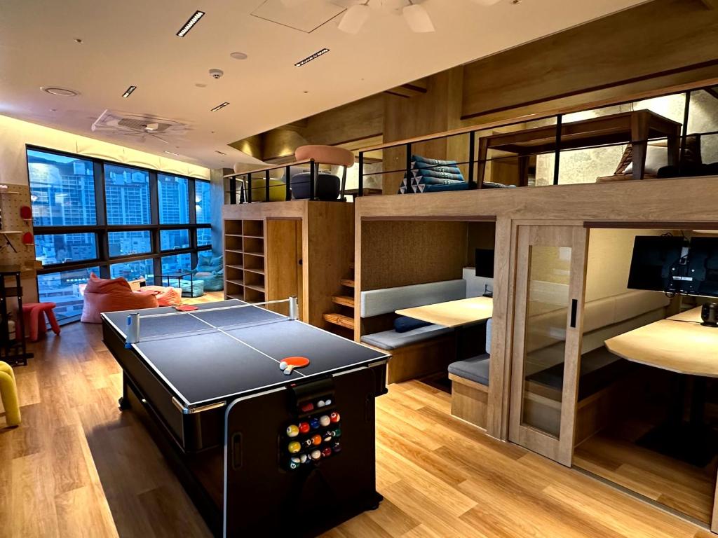 A modern coworking space with a pool table, loft seating, and glass windows overlooking a cityscape at dusk/fall light.