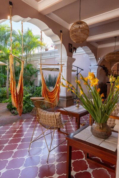 Courtyard patio with orange fabric hammocks, wicker chairs, and potted plants under white arched columns.