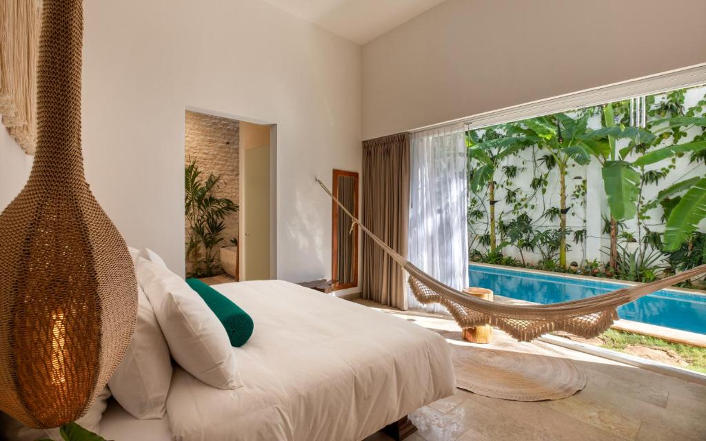 Bright bedroom with a hammock by a large glass wall opening to a blue pool and tropical garden outside.