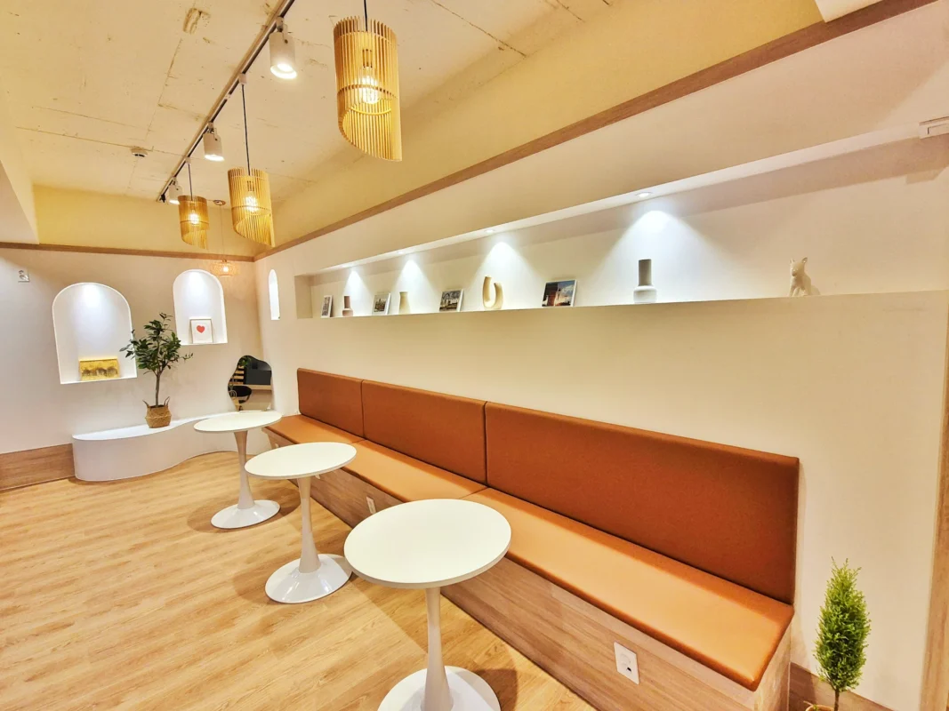 Cozy minimalist lounge with an orange bench along the wall, white round tables, and warm wooden pendant lights.
