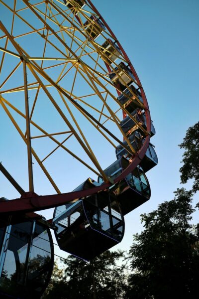 Close-up of a large Ferris wheel with yellow supports and a red rim against a clear blue sky.