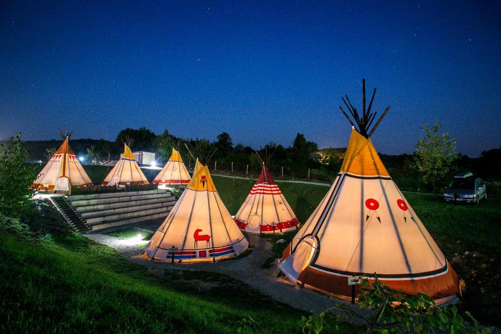Row of illuminated tipi tents arranged on a grassy field at night under a starry sky.