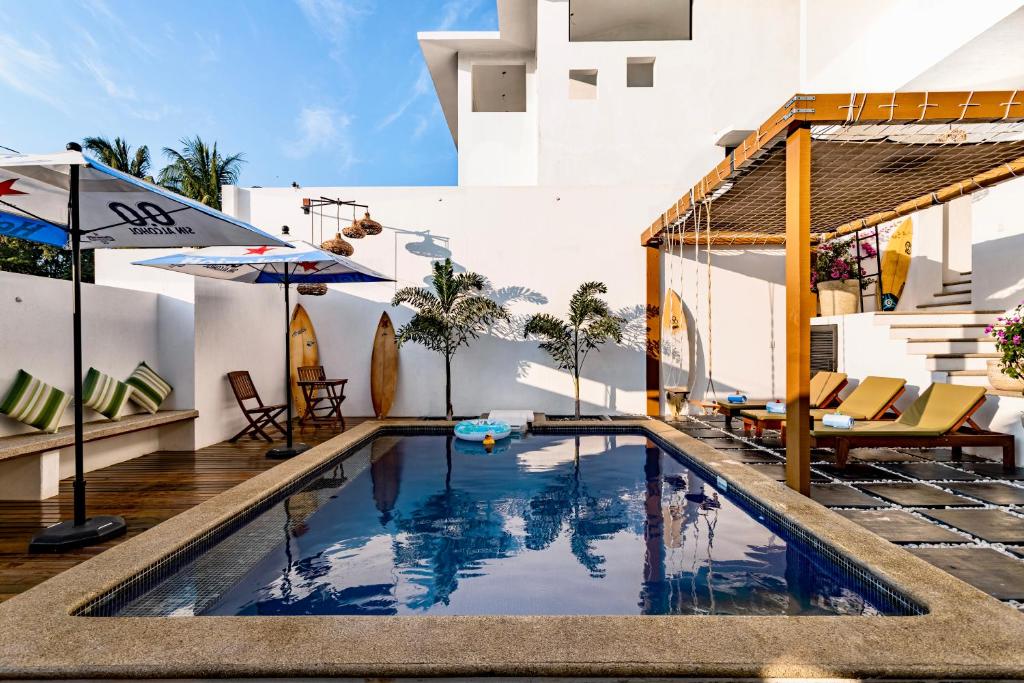 Sunny poolside courtyard with lounge chairs under an orange pergola, surfboards by white walls, and umbrellas for shade.
