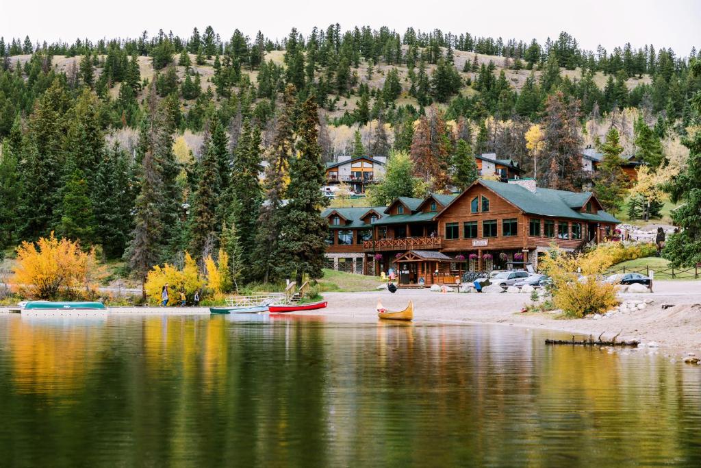 Wooden lakeside lodge with green roof nestled among pine trees; colorful canoes rest on a calm lake shore in autumn light.