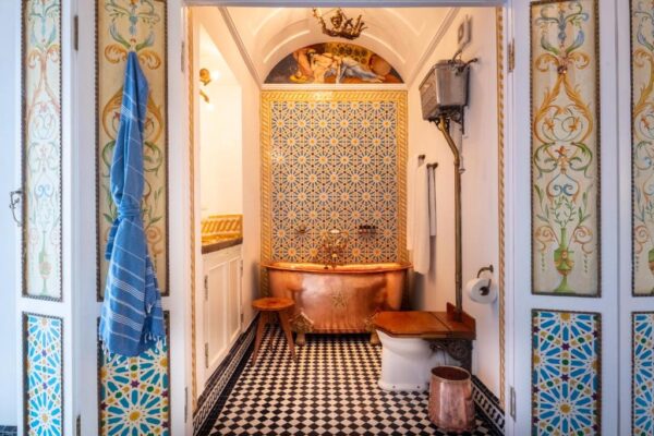 Luxurious bathroom with a copper freestanding tub, checkered black-and-white floor, and ornate mosaic panels on the walls.