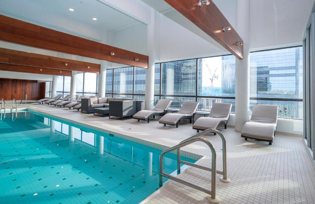 Indoor hotel pool area with turquoise water and a row of lounge chairs along the glass wall