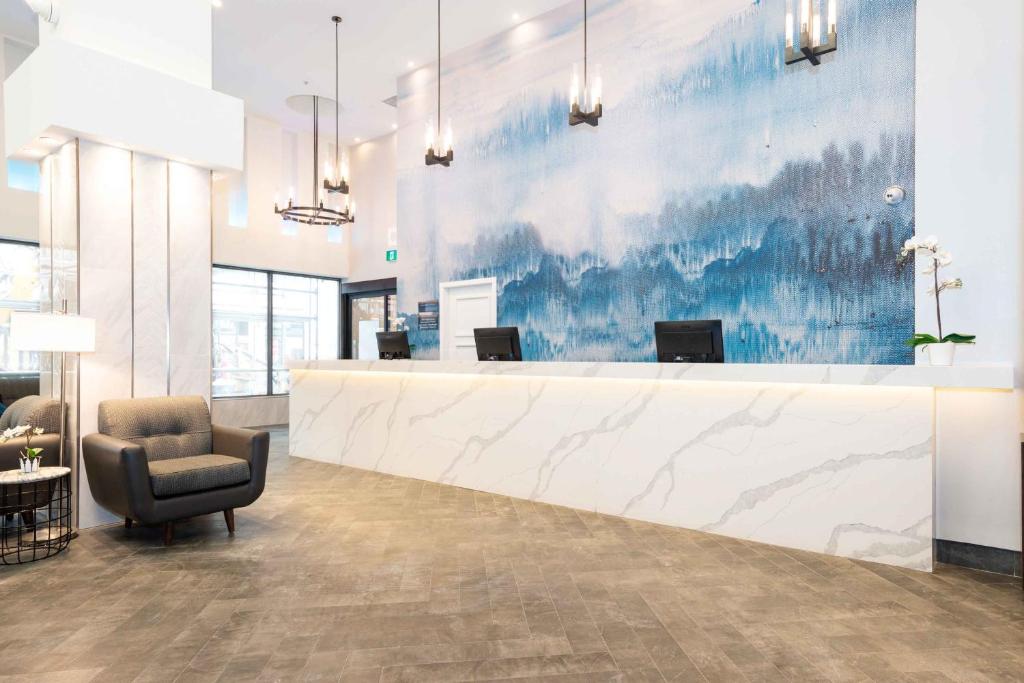 Modern hotel lobby with a white marble-front desk, blue mural wall, and pendant lights overhead.