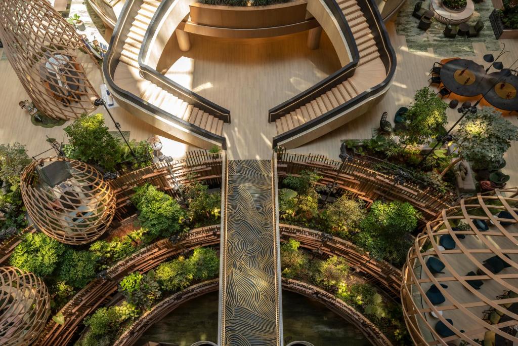 Aerial view of a multi-level wooden spiral walkway surrounding lush greenery in a modern indoor atrium.
