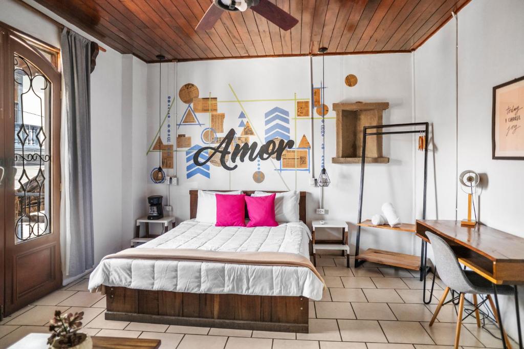 Bed centered in a bright, stylish bedroom with white bedding and two pink pillows under a geometric mural that reads 'Amor'.