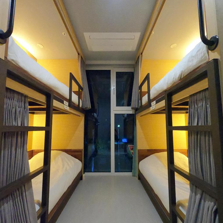 Hostel dorm room with two bunk beds on each side, yellow walls, and a central aisle toward glass doors at the end.