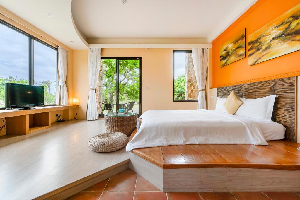 Bright hotel suite with a king bed, orange accent wall, and a wooden platform near a glass door to a balcony.
