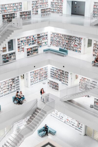 Bright, multi-story library atrium with white shelves, railings, stairs, and people sitting on blue couches reading.