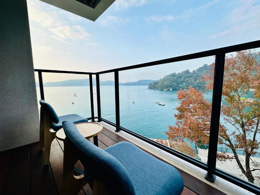 Balcony seating with blue cushioned chairs and a small table overlooking a calm lake with boats and hills in the distance.