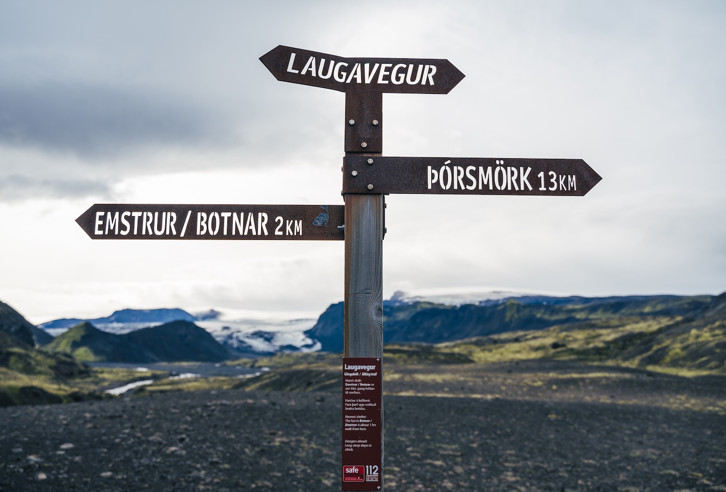 Wooden signpost with arrows reading Laugavegur, Pórsmörk 13 km, and Emstrur/Botnar 2 km, set in a rocky volcanic landscape."