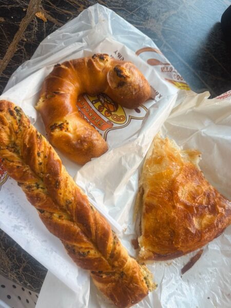 Assorted bakery breads and pastries on parchment, including a ring-shaped loaf, a twisted herb bread, and a flaky cheese pastry piece