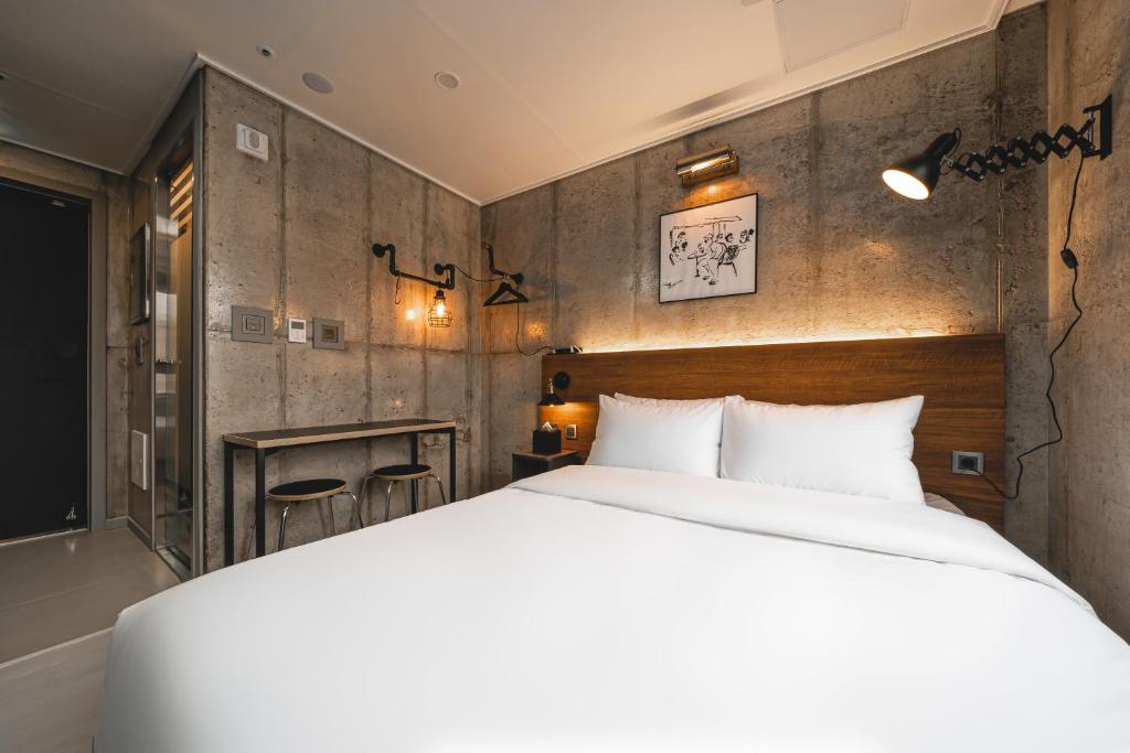 Queen bed in a modern industrial hotel room with a wooden headboard, white bedding, and concrete walls.