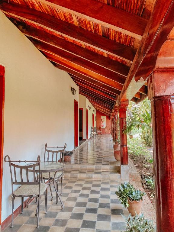 Covered veranda with checkered tile floor, white walls, red doors, and wooden beams; metal chairs along the corridor.