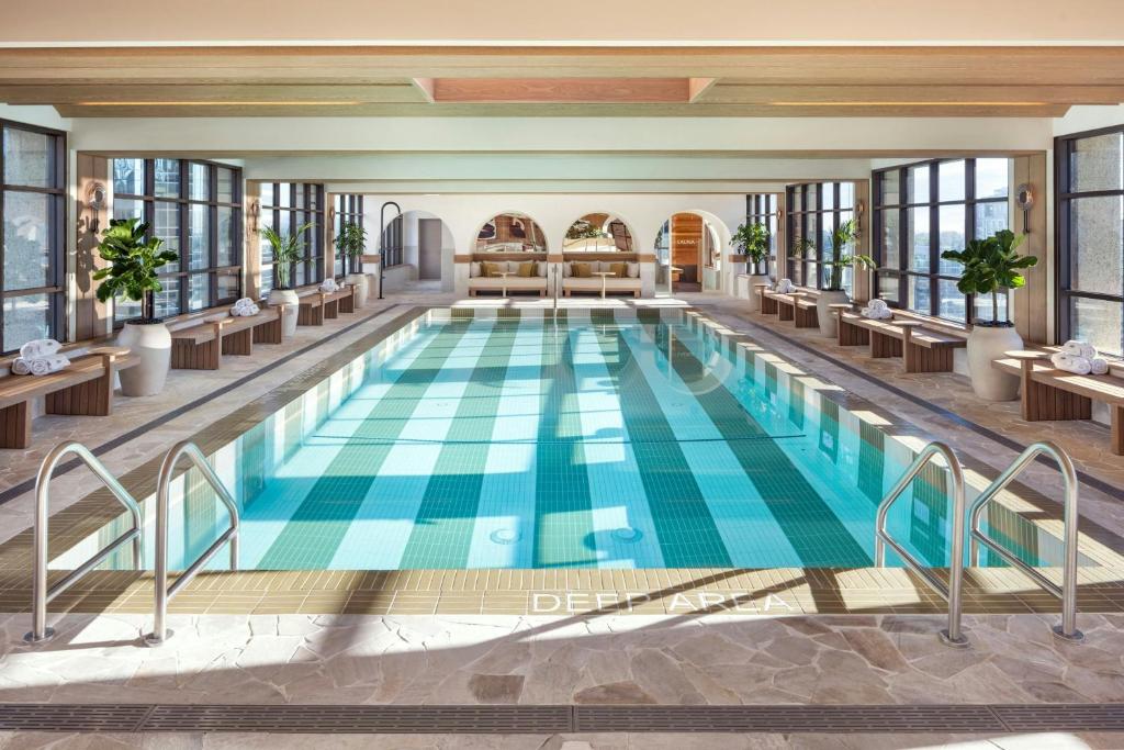 Indoor hotel pool with turquoise water, lounge benches along windows, and potted plants in a bright, airy spa setting.