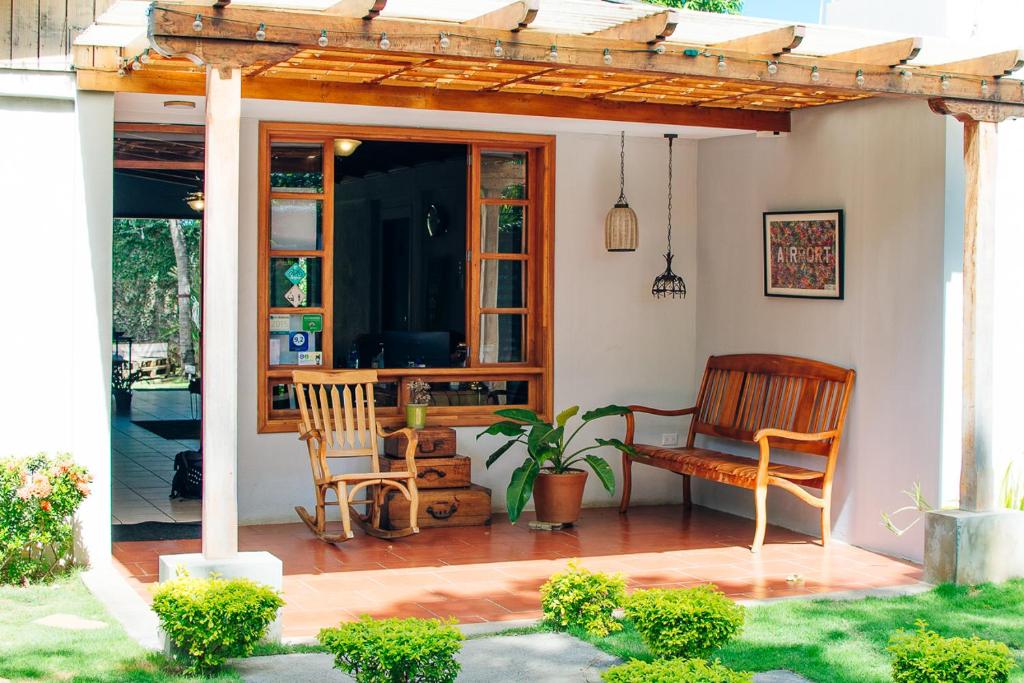 Cozy wooden porch seating area with a bench, chair, potted plant, and hanging lamps, opening into the indoors through a wood-framed window.