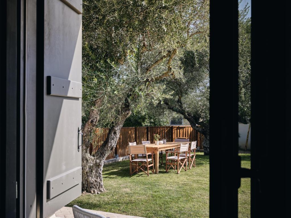 Open doorway looks out onto a sunlit backyard dining area with a wooden table and chairs under olive trees.
