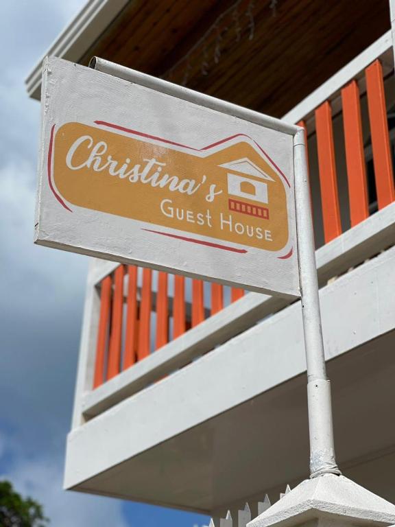 Sign reading Christina's Guest House hanging from a metal post near an orange-railed balcony.