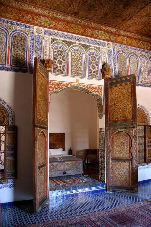 Ornate Moroccan-style bedroom alcove with carved wooden doors opened, revealing a bed and small table.