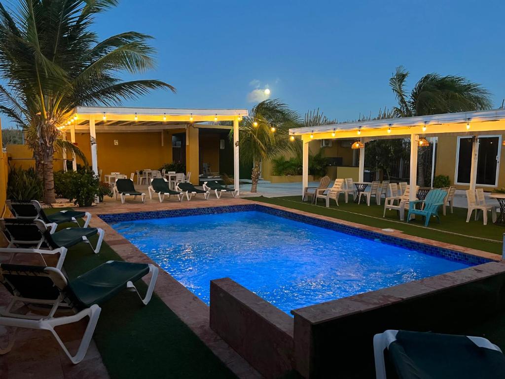Poolside lounge area at dusk with blue swimming pool, palm trees, and string lights over covered seating areas.