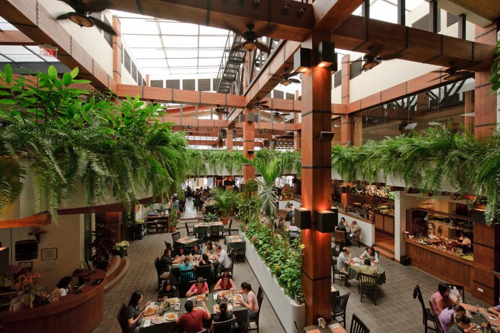 Indoor restaurant atrium with wooden beams, hanging plants, and diners at tables throughout the space.
