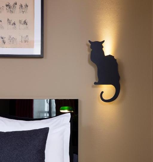 Cat-shaped wall sconce casting a warm glow beside a bed in a bedroom.